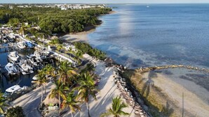An aerial view of a coastal marina with boats docked, a sandy beach, and a rocky shoreline. - Key Largo Villa, Kawama P6, 3/3 (Key Largo)
