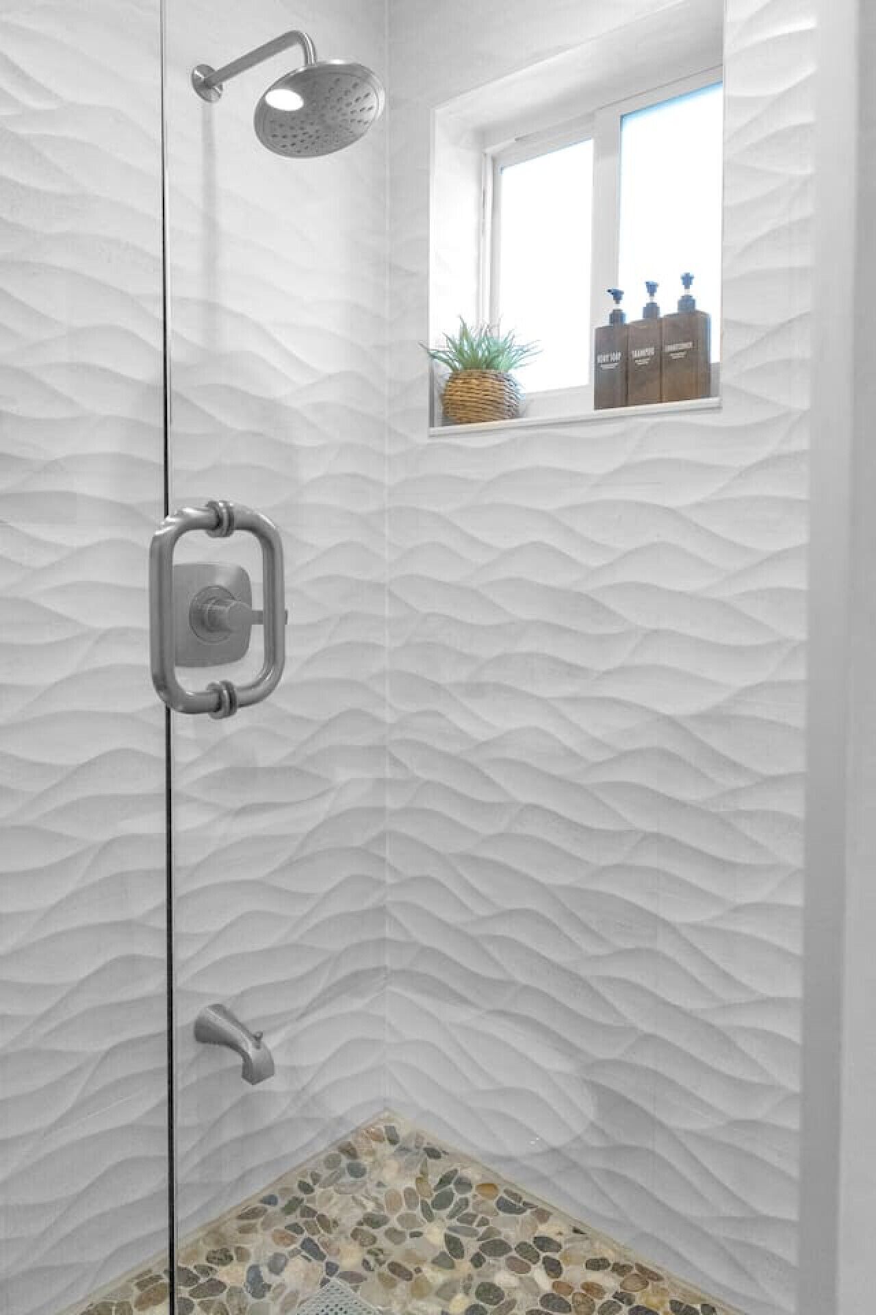 A shower with a textured wall, a window with a plant, and a shelf with toiletries.