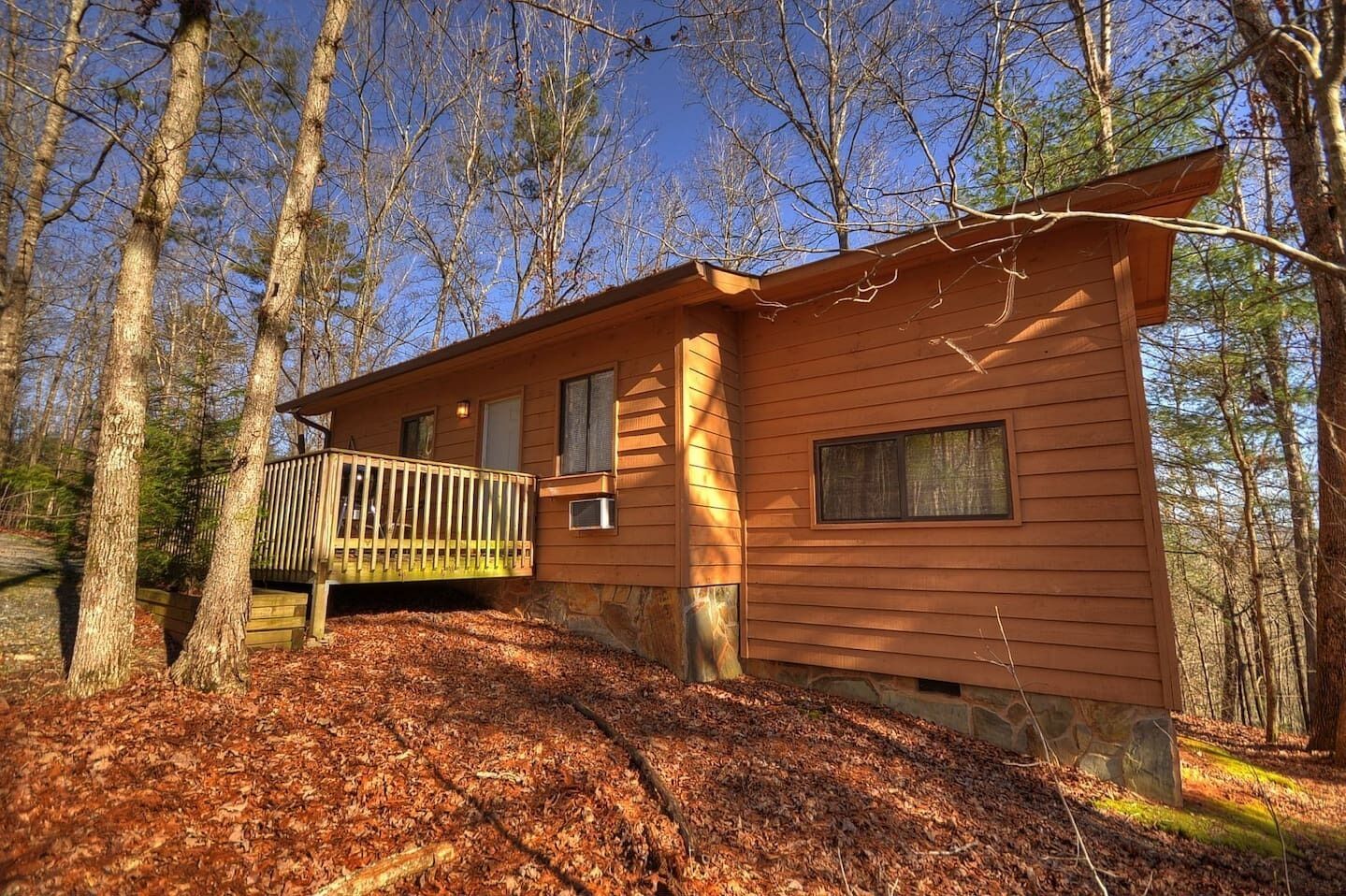 A cabin with a wooden deck, surrounded by trees.