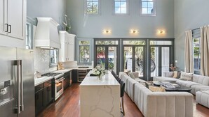 A spacious kitchen with a central island, a dining area, and a living room with a large sofa. - Designer Home on Magazine | Pool and Spa (New Orleans)
