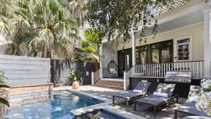 A backyard with a swimming pool, lounge chairs, a grill, and a covered patio area. - Designer Home on Magazine | Pool and Spa (New Orleans)