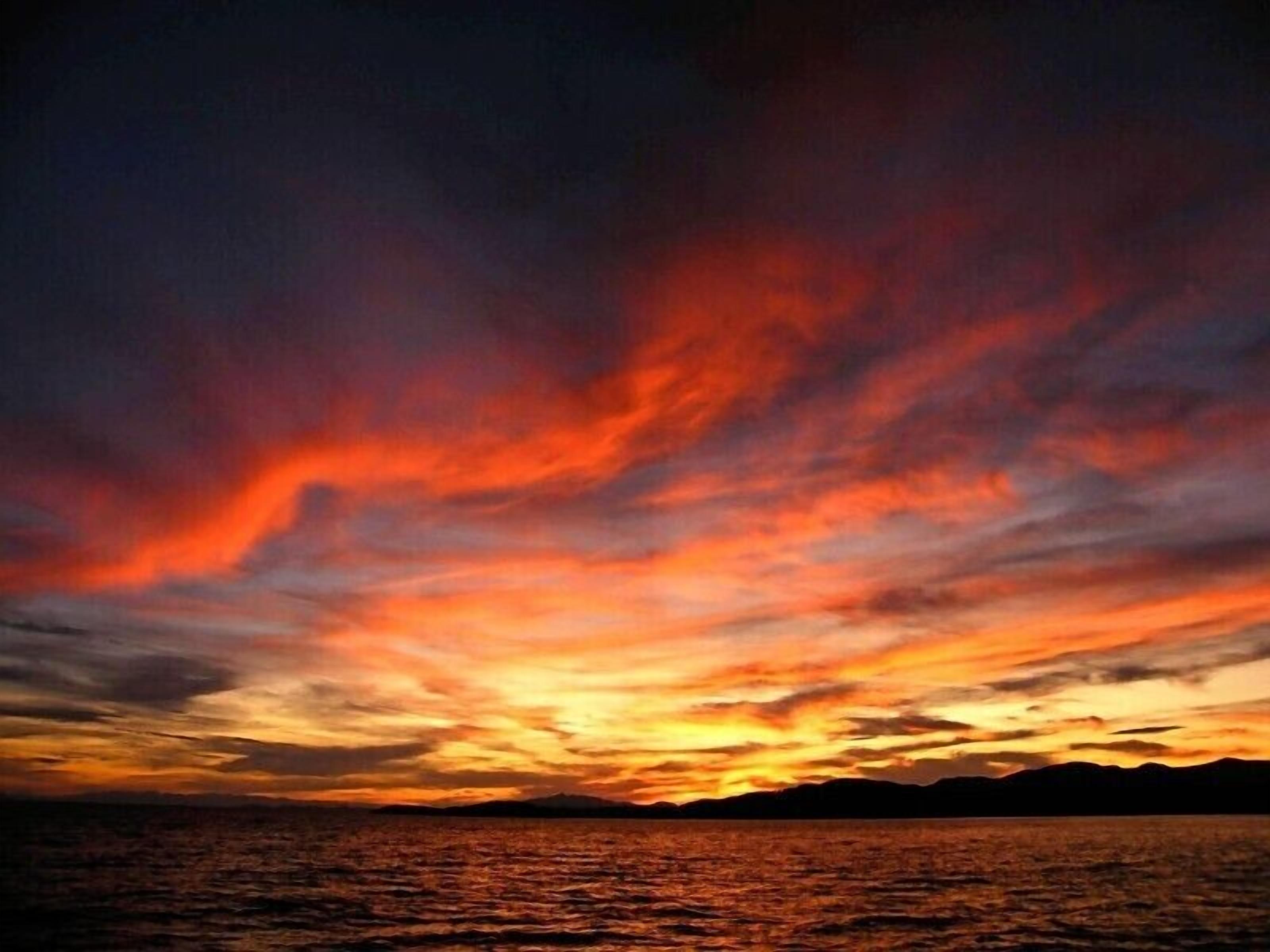 Un tramonto su uno specchio d'acqua, con la sagoma di montagne all'orizzonte.