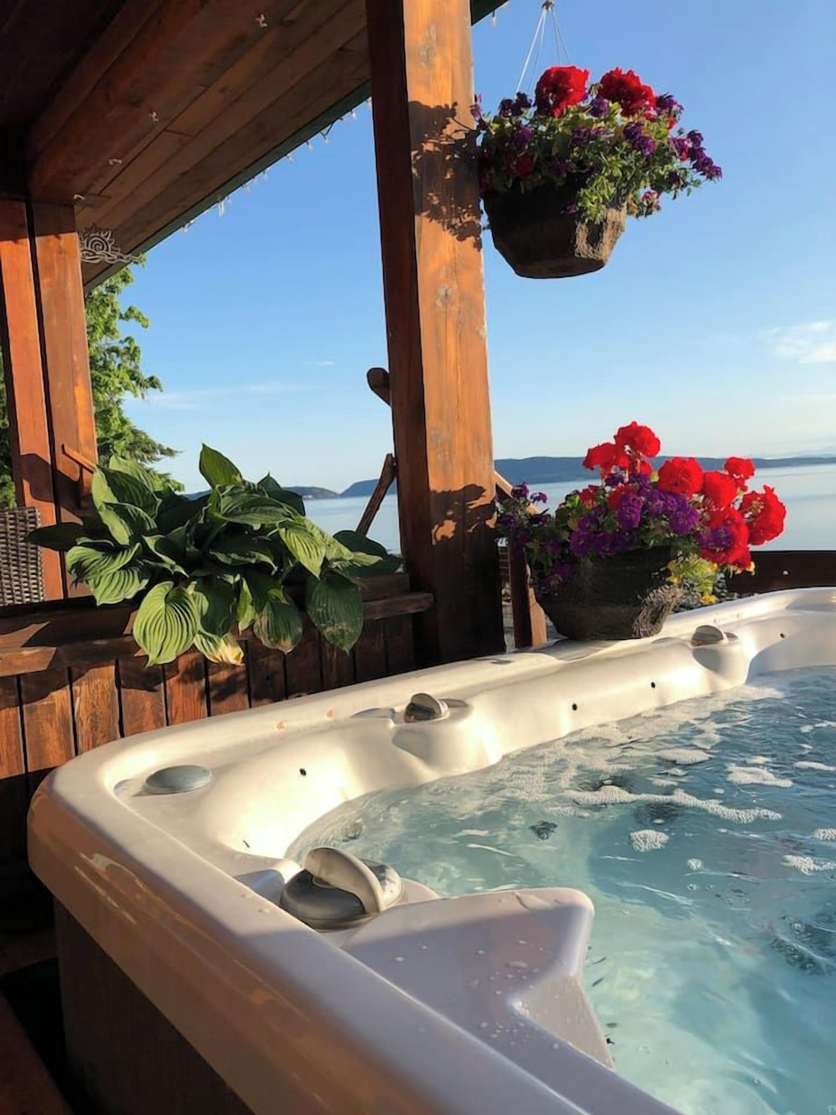 Un bain à remous avec une terrasse en bois et un panier à fleurs suspendu.