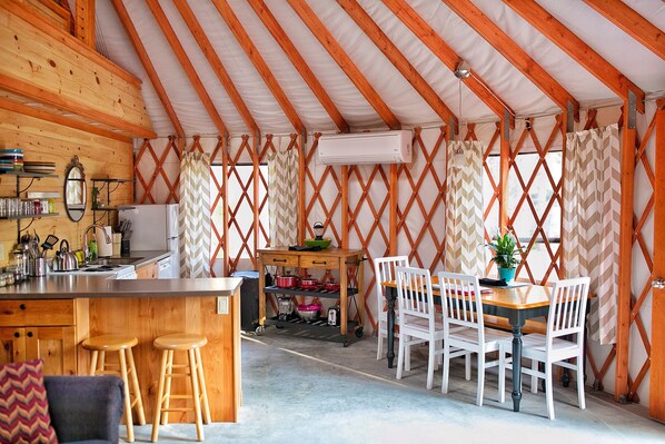 A cozy, well-lit tent-style room with a wooden interior, a kitchen area with a sink and utensils, and a dining table with chairs.