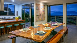 A modern kitchen with a bar area, a dining table set for four, and large windows offering a view of the mountains. - 6BR Luxury Contemporary Villa • Private Pool • Game Room • Quiet Setting (Manuel Antonio)