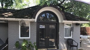 A house with a dark front door, two windows, and a covered patio area with a chair and a potted plant. - GUEST HOUSE 1.5 miles to OU CAMPUS (Norman)