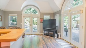 A spacious living area with a large TV, wooden flooring, and a dining table. - GUEST HOUSE 1.5 miles to OU CAMPUS (Norman)