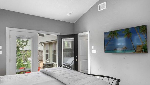 Un dormitorio con cama, un cuadro de una playa y vista a un patio trasero con terraza y una silla.