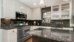 Una cocina moderna con armarios blancos, electrodomésticos de acero inoxidable, encimera de granito y salpicadero oscuro.