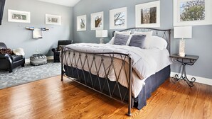 Un dormitorio con cama, una silla, una mesita de noche y cuadros en la pared.