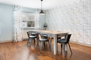 A dining area with a wooden table and four chairs, a window with curtains, and a wall with a birdcage pattern.