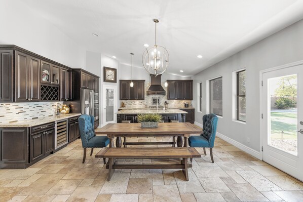 A spacious kitchen with dark cabinetry, a large island, and a central dining table with blue chairs. - Luxurious Family Rental w/ Heated Pool and sport court (Scottsdale)