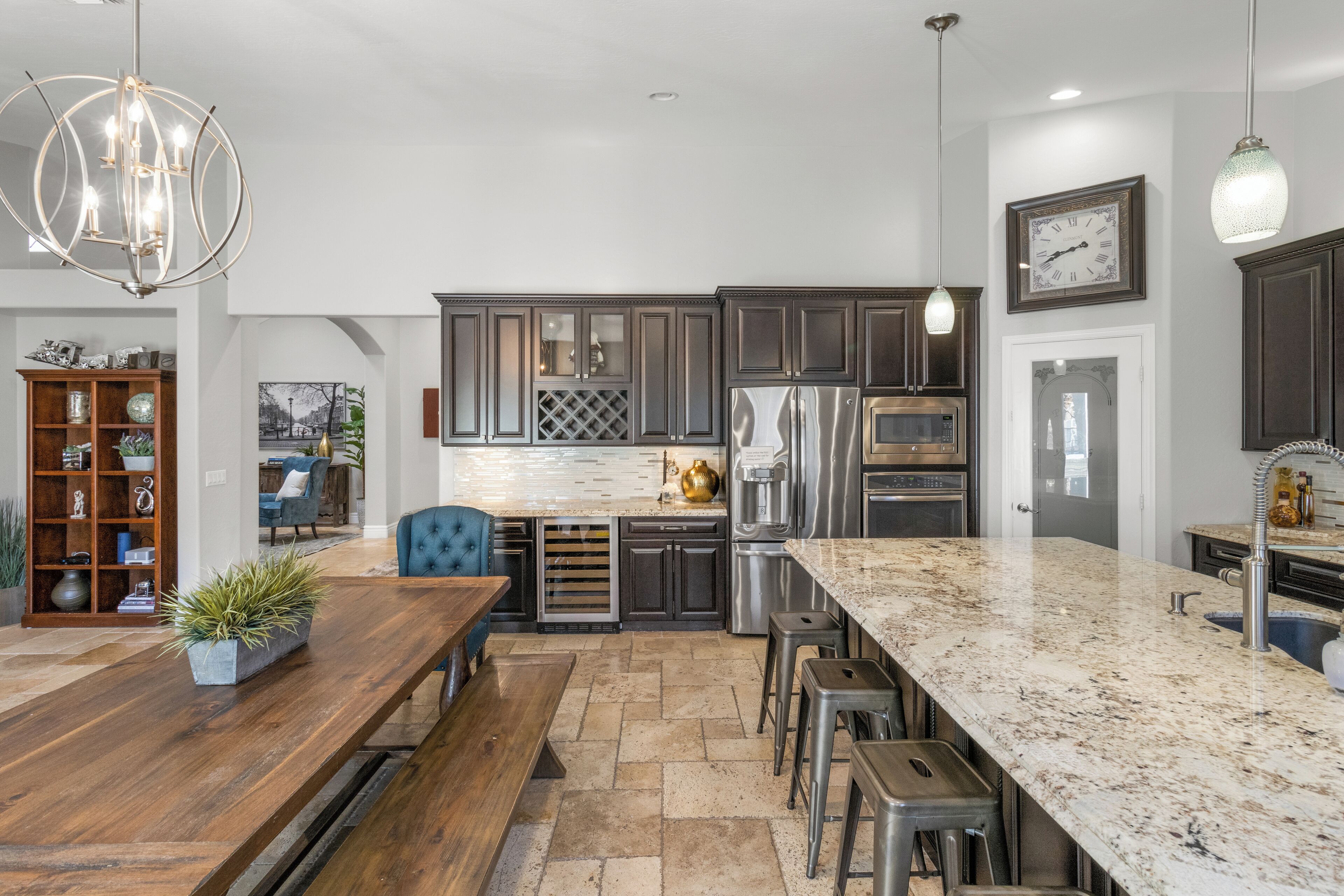 A modern kitchen with dark cabinets, stainless steel appliances, a marble countertop, and a dining area with a wooden table and bar stools.