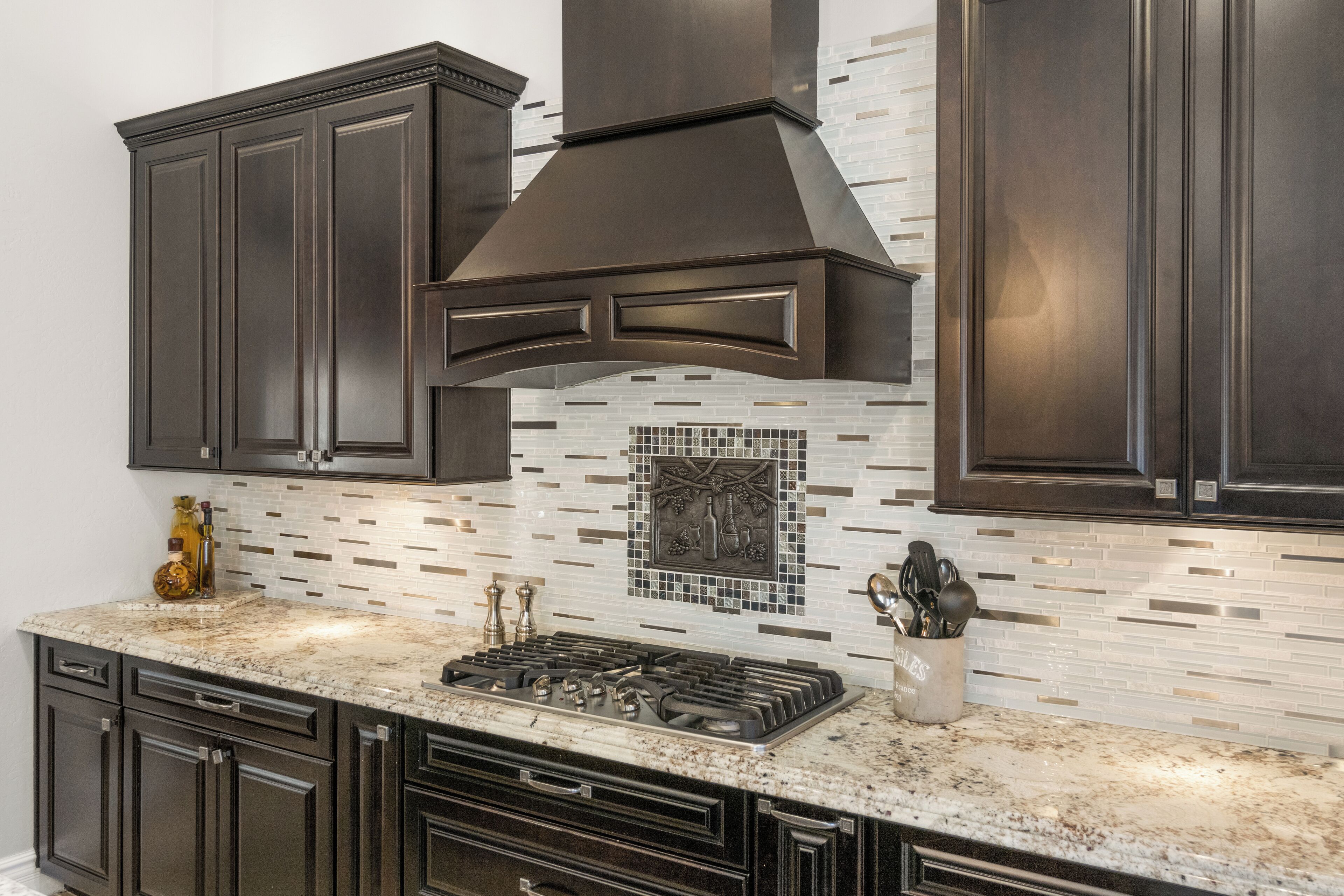 A modern kitchen with dark cabinetry, a stainless steel range hood, and a tiled backsplash.