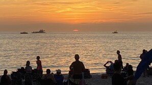 Un coucher de soleil sur l’océan, avec des bateaux et des gens sur la plage.