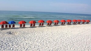 A beach with rows of red and blue umbrellas and beach chairs. - Beach Colony West 8E Beautiful Gulf Views from over sized balcony (Navarre)