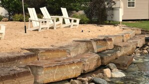 Un muro de piedra con una piscina y sillas blancas al fondo.
