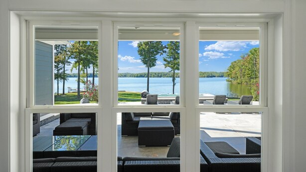 Vista a través de una ventana de un patio con mobiliario exterior y un lago.