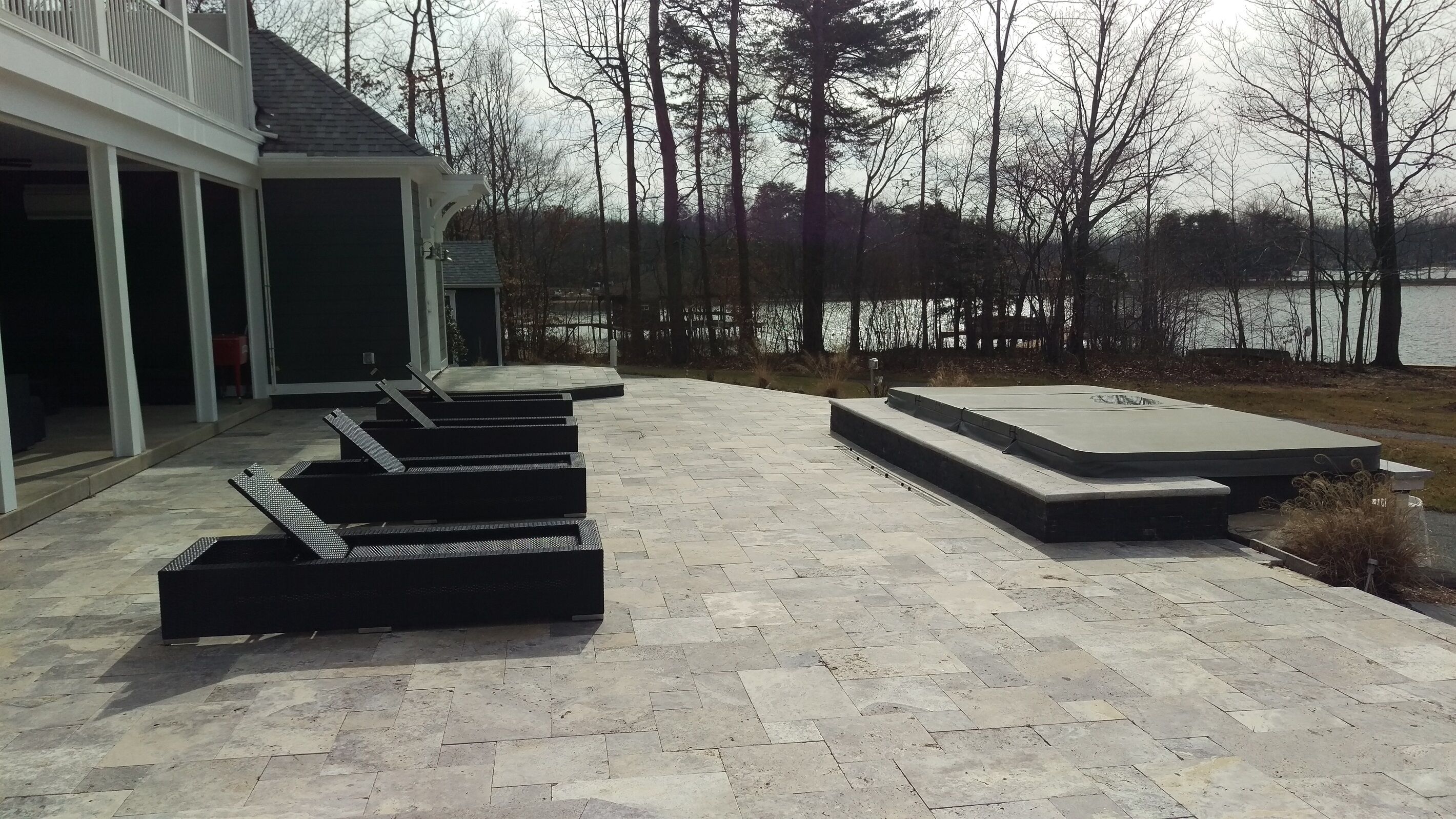 Un patio con suelo de piedra y mobiliario exterior, con vistas a un cuerpo de agua y árboles.