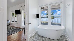 Un baño con una bañera independiente, un ventanal con vistas al exterior y un televisor de pantalla plana montado en la pared.