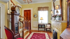 A traditional interior with a wooden staircase, a red armchair, a vintage clock, and a fireplace with decorative lamps.