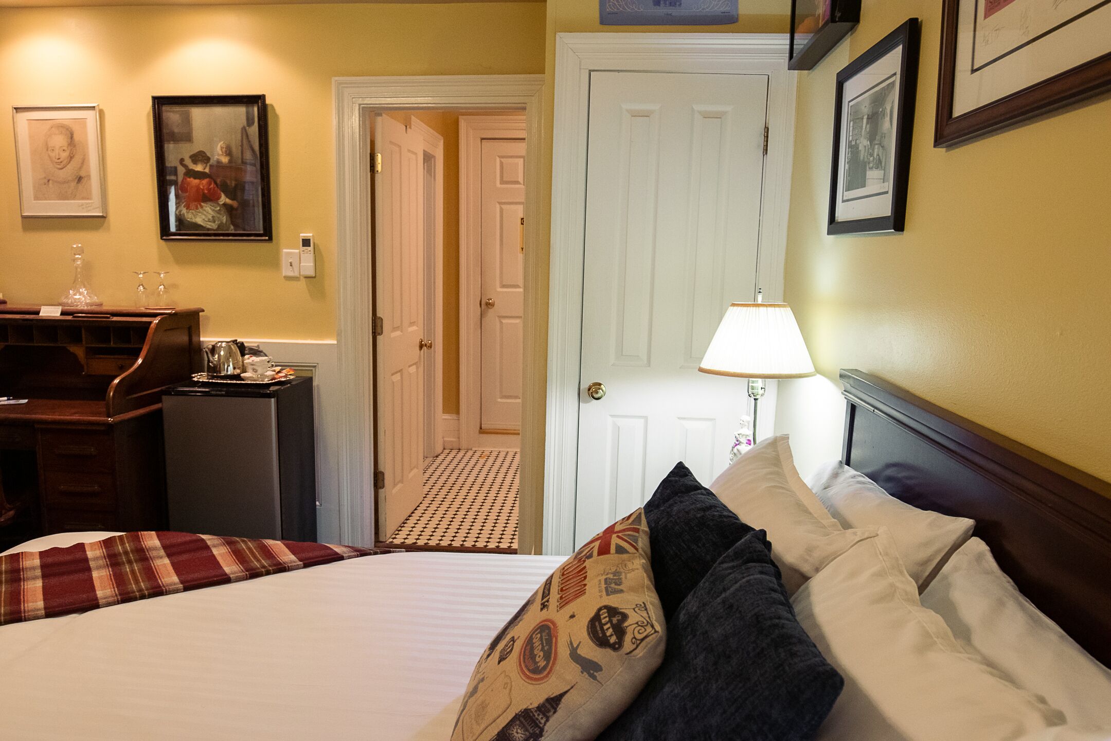 Una habitació d'hotel amb un llit, escriptori, làmpada i una porta.