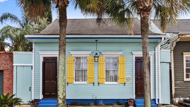 A two-story house with a blue exterior, yellow shutters, and a front porch with potted plants.