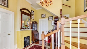 A hallway with a wooden staircase, a red carpet, and a fireplace.