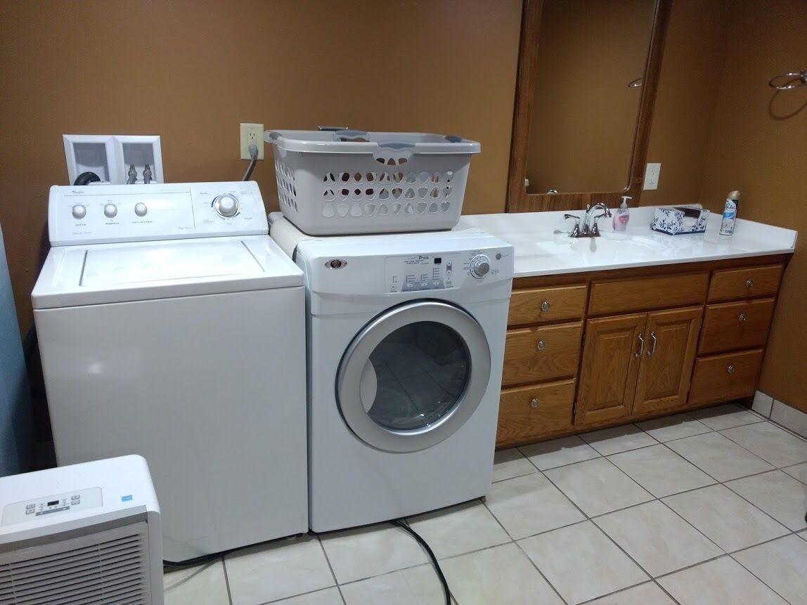 Un espace buanderie comprenant un lave-linge et un sèche-linge à chargement frontal, une machine à laver, un appareil de séchage et un évier avec des articles de toilette.