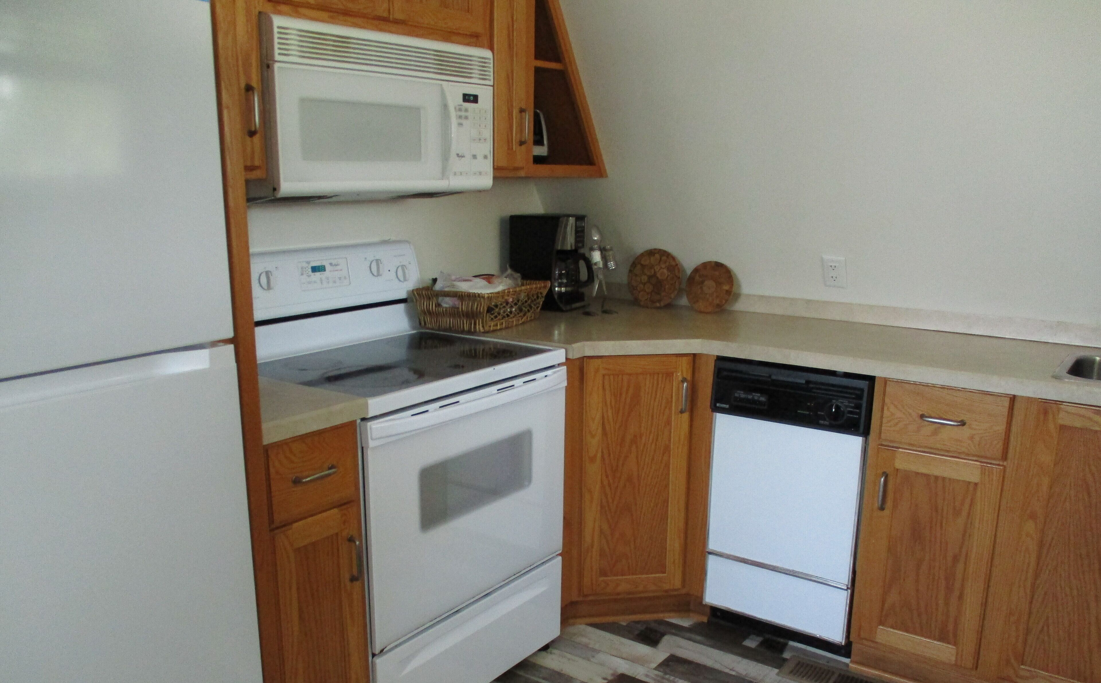 A compact kitchen with white appliances, wooden cabinets, and a tiled backsplash.