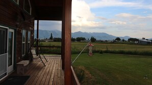 En træterrasse med udsigt til bjerge og en rød fuglebur i det fjerne.