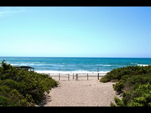 Un sentiero sulla spiaggia che conduce verso l'oceano, con una recinzione in legno e un piccolo riparo.