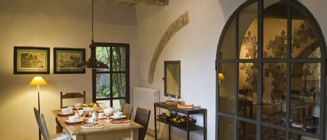 Uma sala de jantar com uma mesa de madeira posta para refeição, uma luminária e quadros nas paredes.