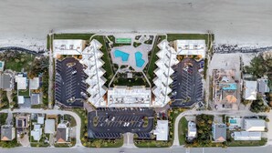 Vista aérea de un hotel costero con una piscina central, varios estacionamientos y un paseo marítimo frente a la playa.