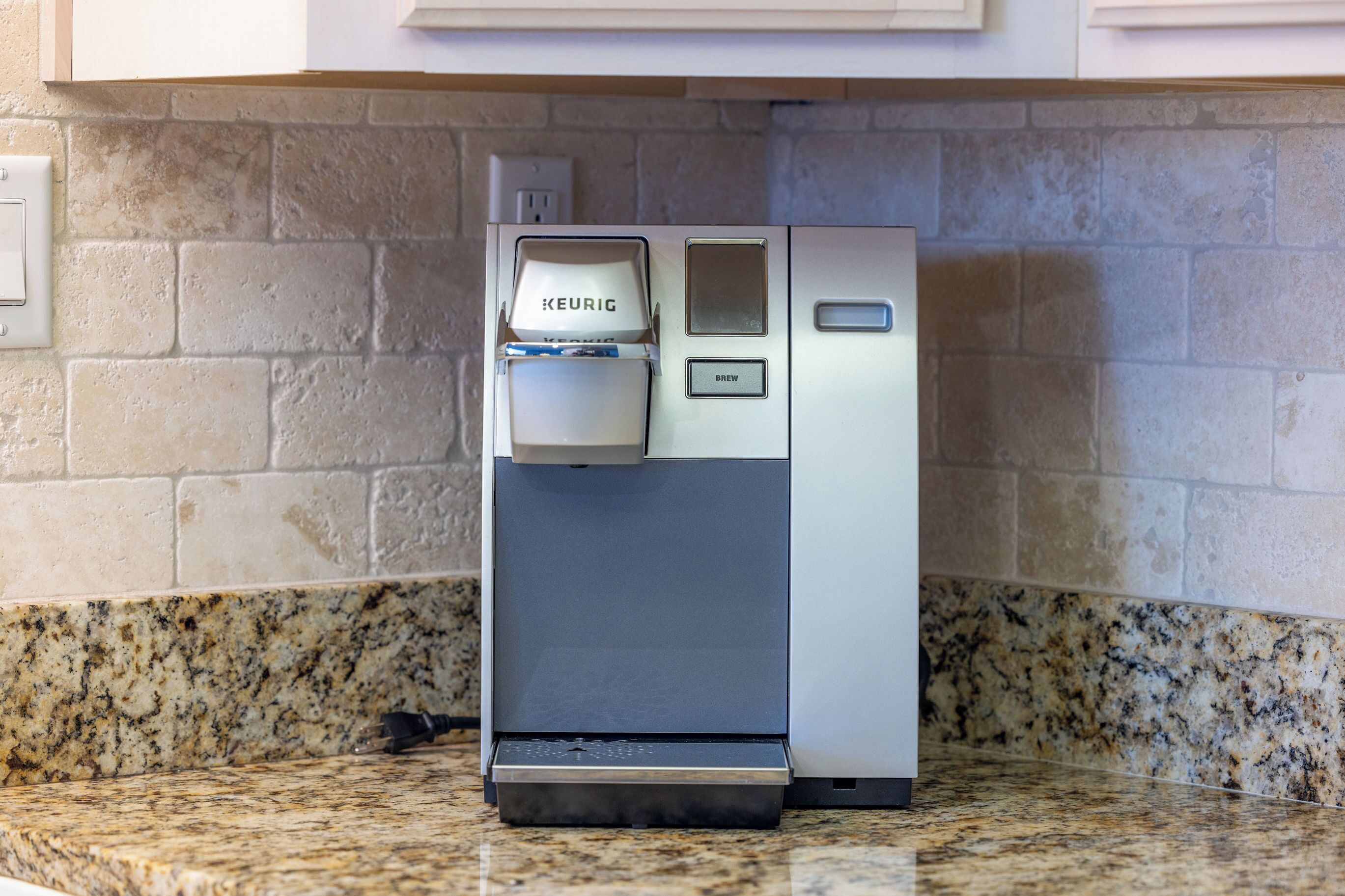 Une machine à café de la marque Keurig, dotée d’un bouton de préparation et d’un réservoir à eau, posée sur un comptoir en granit.