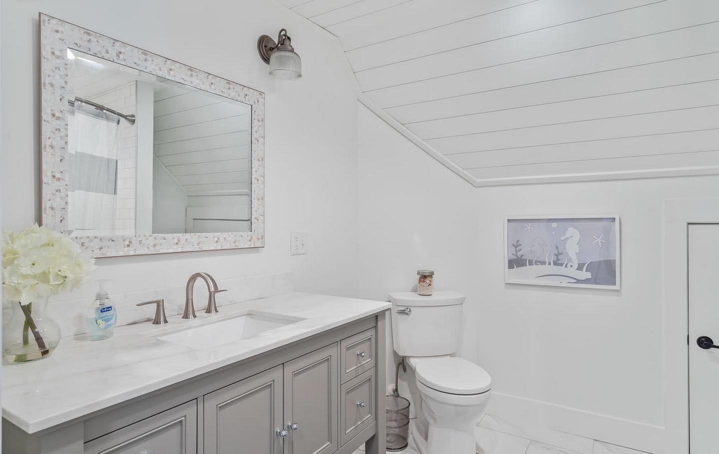 A bathroom with a white vanity, a large mirror, a toilet, and a framed picture on the wall.