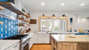 Une cuisine moderne avec des meubles blancs, un pare-feu bleu à motifs, un îlot central et une fenêtre donnant sur un jardin.