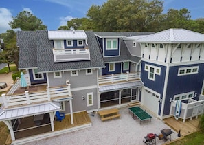 A two-story beach house with a deck, outdoor seating, and a ping pong table.