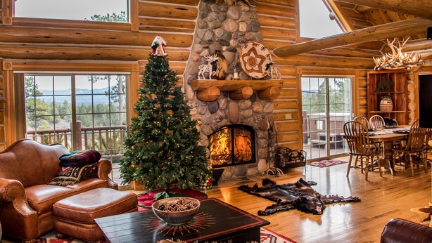 A cozy log cabin interior with a fireplace, a Christmas tree, leather furniture, and a dining area. - Luxury Log Home with Hot Tub on 7+ Acres Featured In Log Home Digest. Sleeps 10 (Pagosa Springs)