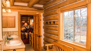 A log cabin interior with a wooden bench, a large window, and a bathroom with a sink and mirror. - Luxury Log Home with Hot Tub on 7+ Acres Featured In Log Home Digest. Sleeps 10 (Pagosa Springs)