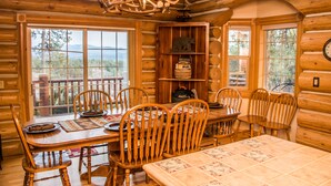 A wooden cabin interior with a dining table, chairs, a chandelier, and large windows offering a view of the outdoors. - Luxury Log Home with Hot Tub on 7+ Acres Featured In Log Home Digest. Sleeps 10 (Pagosa Springs)