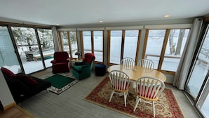 A spacious room with large windows, a wooden dining table with white chairs, a red armchair, a green armchair, and a black sofa.