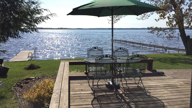 A deck with a table and chairs, an umbrella, and a view of a lake.