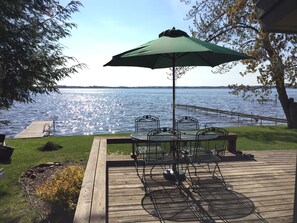 A deck with a table and chairs, an umbrella, and a view of a lake.