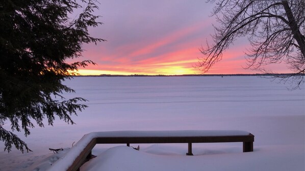 A bench in a snowy landscape with a sunset in the background.