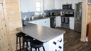 Una cocina con gabinetes blancos, encimera de granito, electrodomésticos de acero inoxidable y piso de madera.