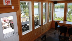 Una habitación con grandes ventanales que dan a un lago, paredes de madera y una mesa con sillas.