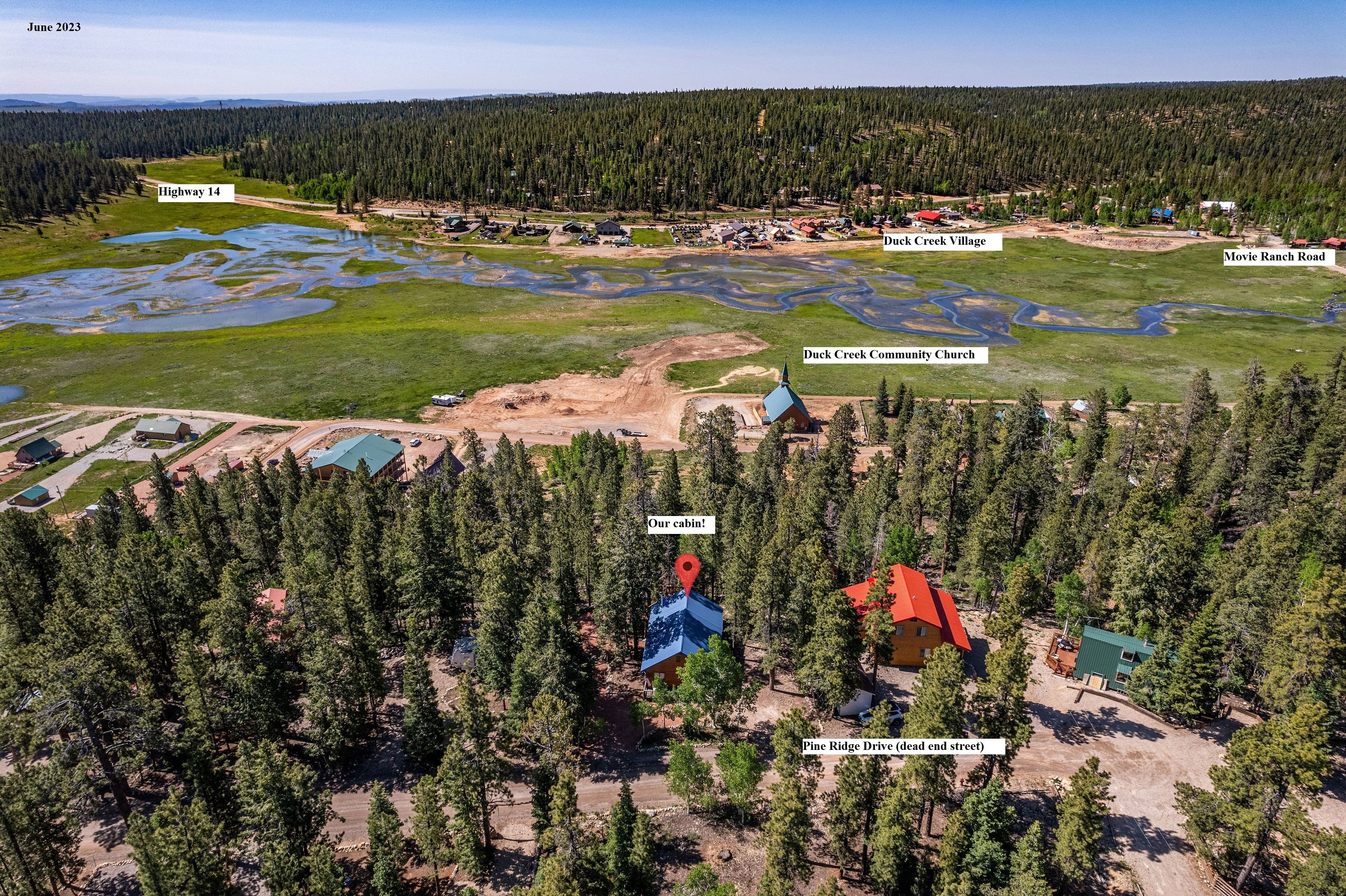 An aerial view of a rural area with a cabin labeled "Our cabin!" surrounded by dense forest, a community church, and a community hall.