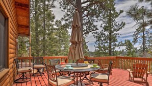 A wooden deck with a round table and chairs, surrounded by Adirondack chairs, and a large umbrella.