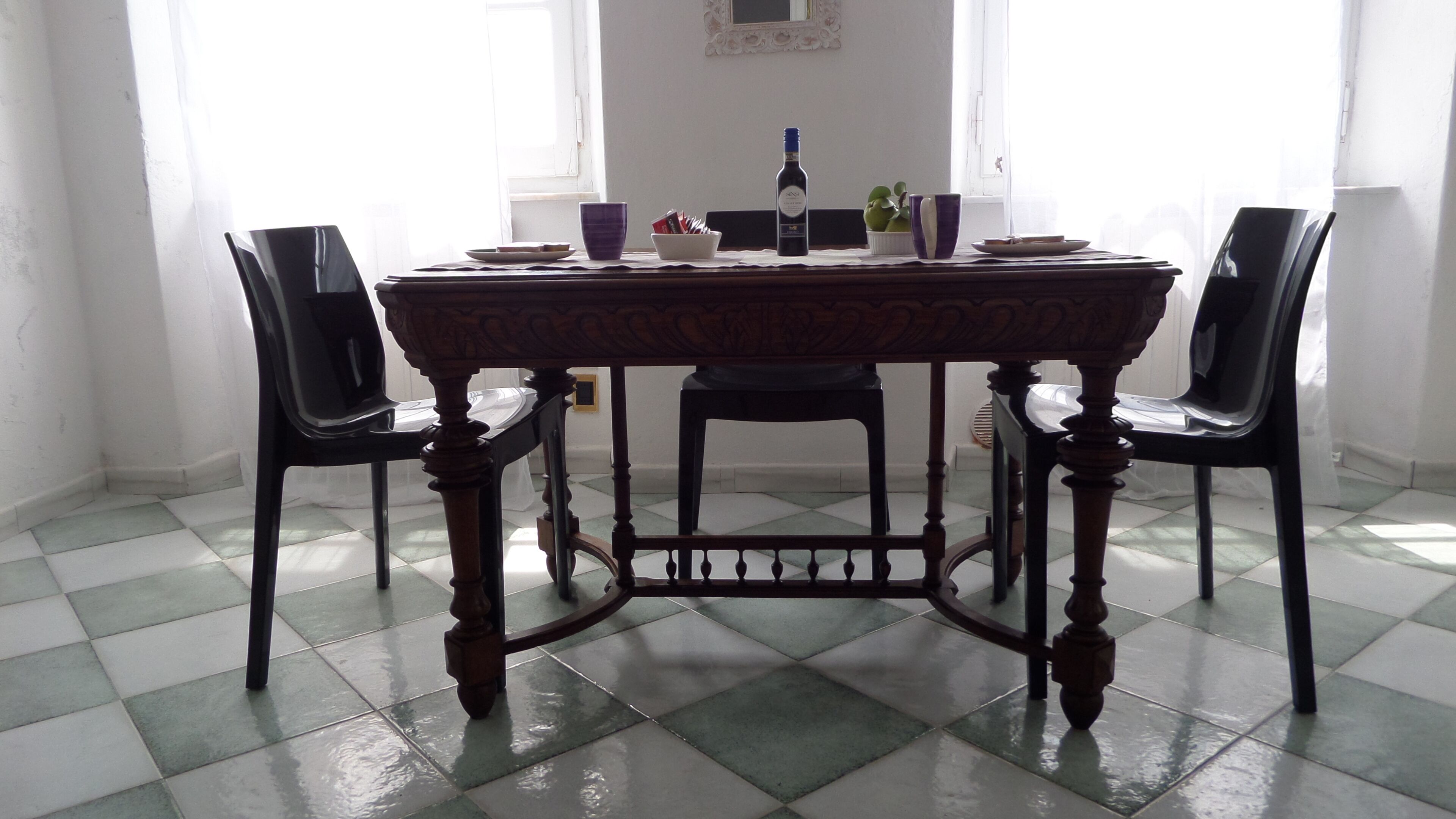 A dining table with chairs, a bottle, and a bowl on a tiled floor.